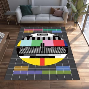 May include: A rectangular rug with a retro TV test signal design. The rug has a grey background with a grid pattern and a large circular graphic with colourful bars and the text "NO SIGNAL".