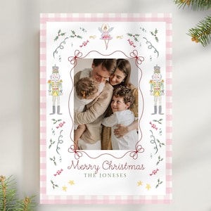 May include: A rectangular Christmas card featuring a light pink and white gingham border. The center displays a photograph of a family surrounded by watercolor illustrations of nutcrackers, a fairy, holly, and candy. Text reads Merry Christmas THE JONESES.