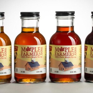 May include: Four glass bottles of maple syrup with black caps. Each bottle has a label with the text "Maple Farmers" and a picture of a small house. The bottles contain syrup of varying shades of amber and red, each bottle is 8 oz.