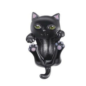 May include: A black cat figurine with green eyes and pink accents on the ears and paws. The cat is in a playful pose, with its paws outstretched and tail curled. The figurine has a glossy finish.