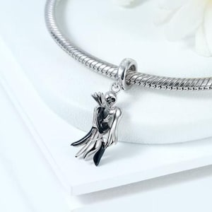 Puede incluir: Un charm de plata con una pareja de esqueletos abrazándose. El charm tiene detalles en negro y plata y está suspendido de una cadena de plata. La pareja de esqueletos es el punto focal, con detalles esqueléticos.