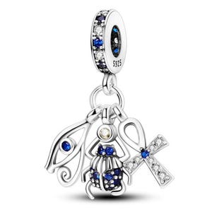 May include: A silver charm with three dangling pendants. The charm features a scarab beetle, an ankh, and an eye of Horus, all adorned with blue and clear gemstones. The top ring is embellished with blue and clear stones and has the text "S925".