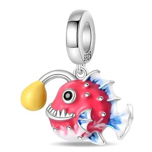 Può includere: Un charm in argento con un design di pesce rana rosso, bianco e blu. Il pesce ha un'esca gialla e un viso dettagliato con un sorriso dentuto. Il charm è contrassegnato con "S925".
