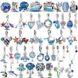 Könnte beinhalten: Eine Sammlung von silberfarbenen Metallanhängern mit ozeanischen Motiven, darunter Meeresschildkröten, Kraken, Seesterne, Muscheln, Kreuzfahrtschiffe, Delfine und Wale, viele verziert mit blauem, rosa und grünem Emaille sowie klaren Kristallen.