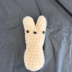 May include: A crocheted plush bunny toy with a light peach color and black eyes.