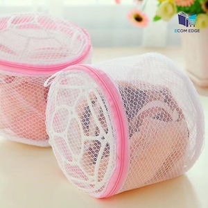 May include: Two white mesh laundry bags with pink zippers and trim. The bags are cylindrical and appear to be filled with clothing. The bags are designed to protect delicate items during washing.