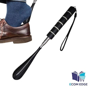May include: A black shoe horn with a long handle and a black and white padded grip. The shoe horn is being used to help put on a brown leather shoe. A black lanyard is attached to the handle.