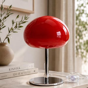 May include: A table lamp featuring a glossy, vibrant red mushroom-shaped shade supported by a polished chrome cylindrical stem and a circular chrome base. The lamp includes a clear power cord with an inline switch, showcasing a sleek design.