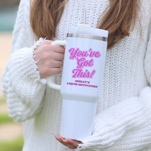 Personalized 40 oz tumbler with handle and straw featuring “You Got This” motivational message and custom name, held by woman in white sweater next to a snake plant. Custom iced coffee cup for women, ideal gift for her or office.