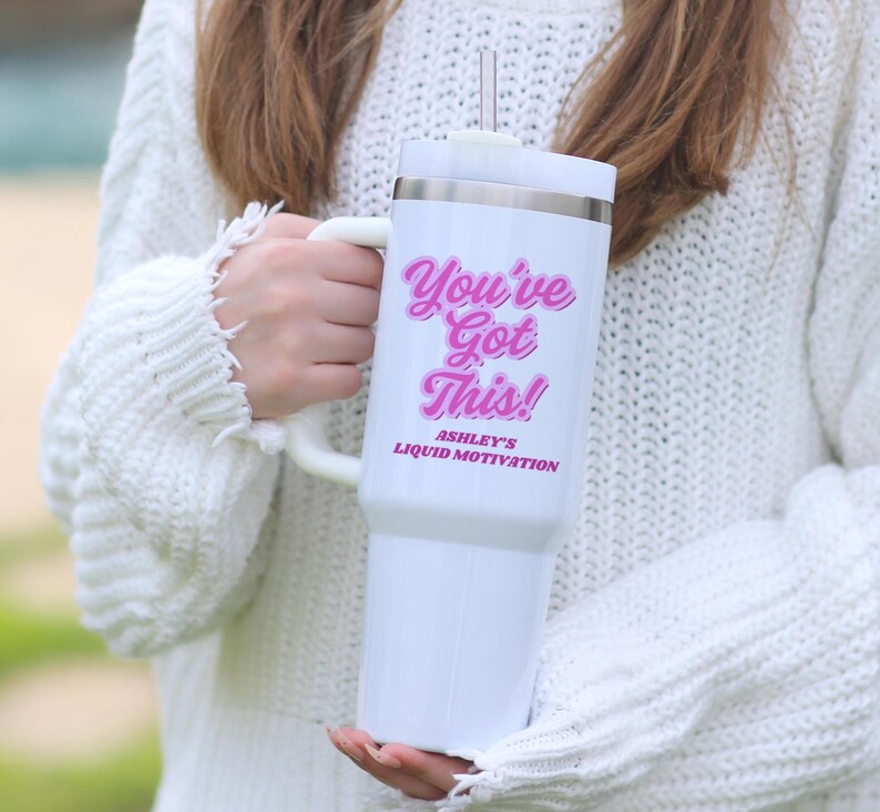 Personalized 40 oz tumbler with handle and straw featuring “You Got This” motivational message and custom name, held by woman in white sweater next to a snake plant. Custom iced coffee cup for women, ideal gift for her or office.