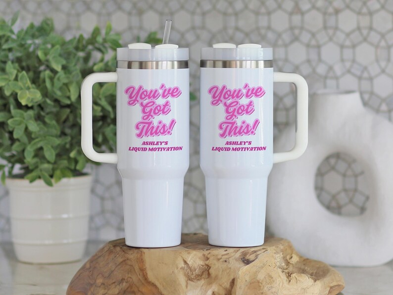 Personalized 40 oz tumbler with handle and straw featuring “You Got This” motivational message and custom name, held by woman in white sweater next to a snake plant. Custom iced coffee cup for women, ideal gift for her or office.