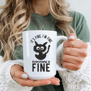 May include: White ceramic mug with a black cat illustration and the text "It's fine. I'm fine. Everything is FINE."