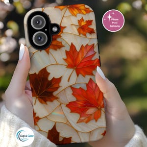 May include: A phone case featuring a design of autumn maple leaves in shades of red, orange, and brown against a cream-colored background. The case has a glossy finish and is held in a person's hands. The case is for iPhone, Pixel, and Samsung phones.