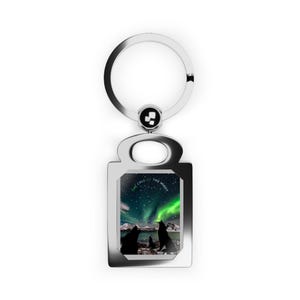 May include: Silver key chain with a rectangular image of three wolves howling at the aurora borealis. The image has the text "The Call of the Night".