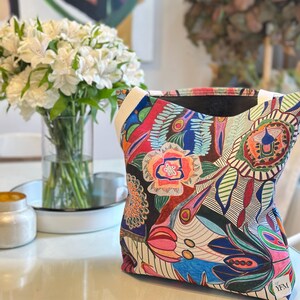 Puede incluir: Una bolsa de tela colorida con un dise&ntilde;o floral y abstracto. La bolsa tiene un forro negro y una correa blanca. La bolsa tiene el texto "YFM" en la esquina inferior derecha.