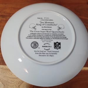 May include: White ceramic plate with a printed image of Joe Montana, a football player, and the text "Joe Montana: King of Comebacks" by Rick Brown. The plate is part of the "The Great Super Bowl Quarterbacks" collection and is officially licensed for trading on the Bradford Exchange. The plate has a Bradford Exchange logo and a NFL logo.