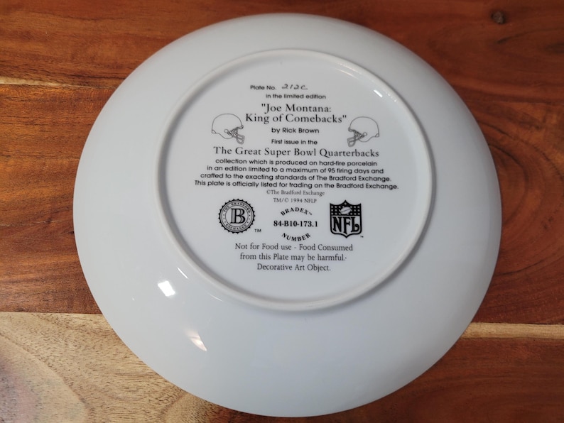 May include: White ceramic plate with a printed image of Joe Montana, a football player, and the text "Joe Montana: King of Comebacks" by Rick Brown. The plate is part of the "The Great Super Bowl Quarterbacks" collection and is officially licensed for trading on the Bradford Exchange. The plate has a Bradford Exchange logo and a NFL logo.