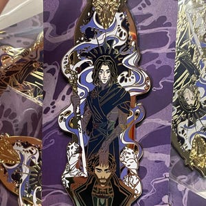 May include: A gold-colored enamel pin featuring a stylized illustration of a figure with long dark hair, holding a staff. The pin has blue and white accents, with the text "THE HERALD OF THE ARCANA" at the bottom. The artist's signature "miraii_art+" is also visible.