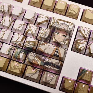 May include: A custom mechanical keyboard with keycaps featuring an anime character design. The keycaps have a cream-colored base with gold accents and illustrations. The Enter, Shift, and Ctrl keys are labeled. The keyboard has a silver frame.