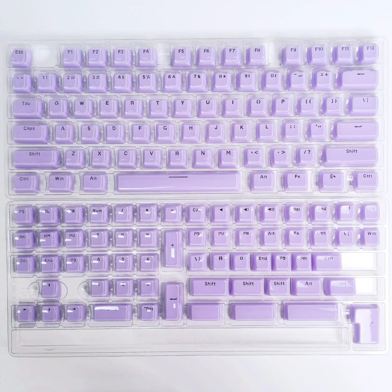 May include: Two keyboard covers with a light purple keycap design. The keycaps are arranged in a standard QWERTY layout, with alphanumeric keys, function keys, and a number pad. The covers are made of a clear material.