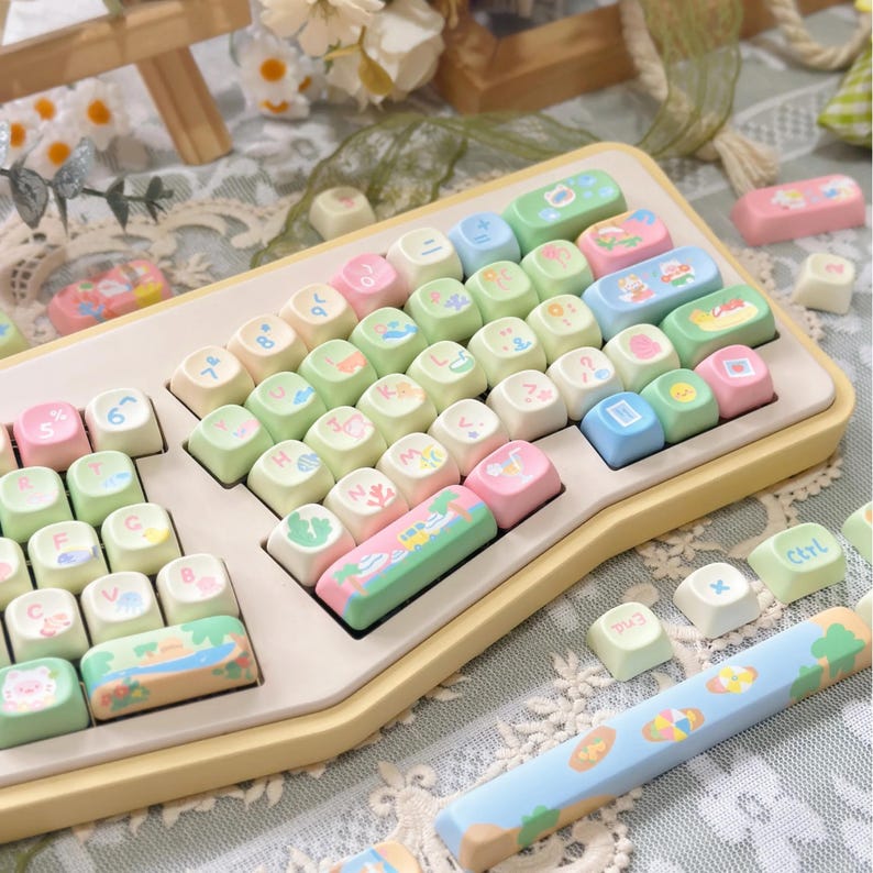 K&ouml;nnte beinhalten: Eine pastellfarbene Tastatur mit individuellen Tastenkappen. Die Tasten sind eine Mischung aus Hellrosa, Gr&uuml;n, Blau und Creme. Einige Tasten zeigen kleine Illustrationen von Landschaften und anderen Designs. Die Tastatur hat einen gelben Rahmen.