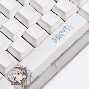May include: Close-up of a white keyboard with a custom keycap featuring an anime character illustration. The keycap has Japanese text and a detailed image of a character with silver hair and pointed ears. The surrounding keys are plain white.