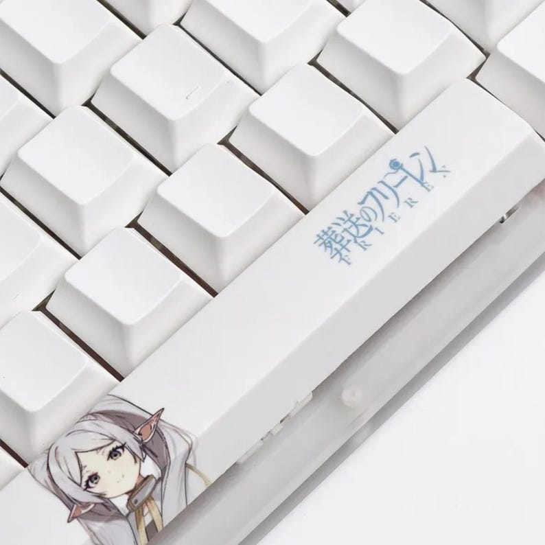 May include: Close-up of a white keyboard with a custom keycap featuring an anime character illustration. The keycap has Japanese text and a detailed image of a character with silver hair and pointed ears. The surrounding keys are plain white.
