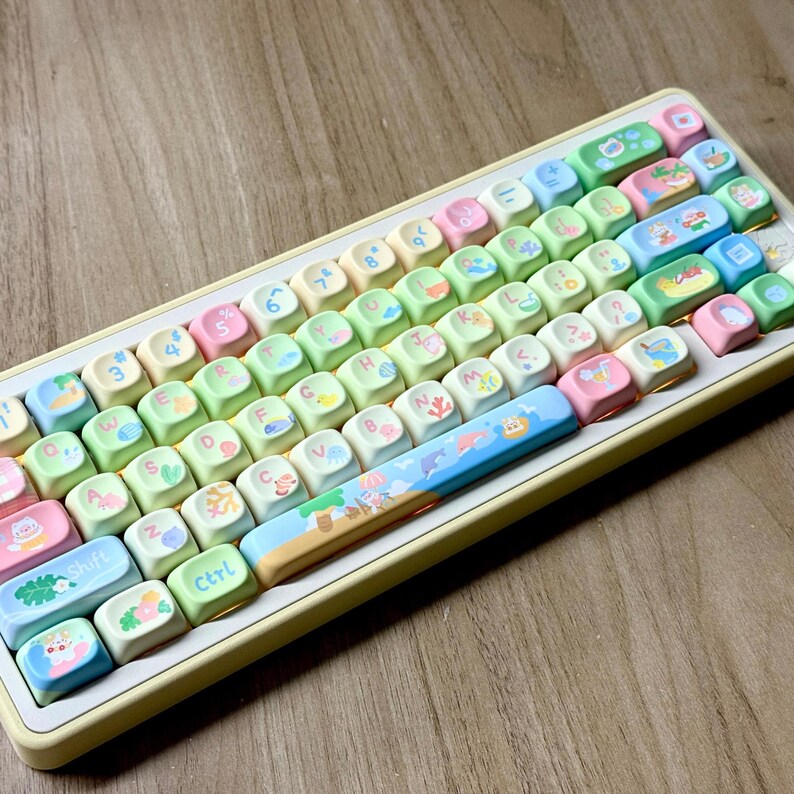 K&ouml;nnte beinhalten: Eine pastellfarbene Tastatur mit individuellen Tastenkappen. Die Tasten sind eine Mischung aus hellgr&uuml;n, rosa und blau, mit verschiedenen Illustrationen. Die Tastatur hat einen gelben Rahmen und ein Standard-QWERTZ-Layout. Die Tastenkappen zeigen Zahlen, Buchstaben und Symbole.