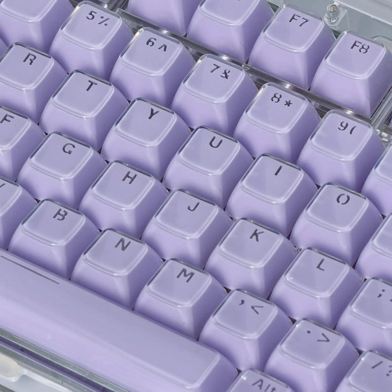 May include: Close-up of a mechanical keyboard with light purple keycaps. The keys are arranged in a standard QWERTY layout, with white lettering and symbols. The keyboard has a clear, transparent frame.