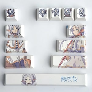 Puede incluir: Un conjunto de teclas de teclado blancas con ilustraciones de estilo anime. Las teclas muestran varias imágenes de un personaje femenino con cabello blanco y un bastón, junto con texto japonés.