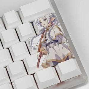 May include: White mechanical keyboard with a custom keycap featuring an anime-style illustration of a female character with long white hair, holding a staff. The keycap is a vibrant accent among the white keys.