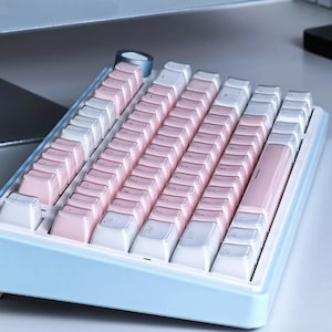 May include: A pastel-colored mechanical keyboard with a light blue frame. The keycaps alternate between white and pink, creating a soft, visually appealing aesthetic. The keyboard is designed for computer use.