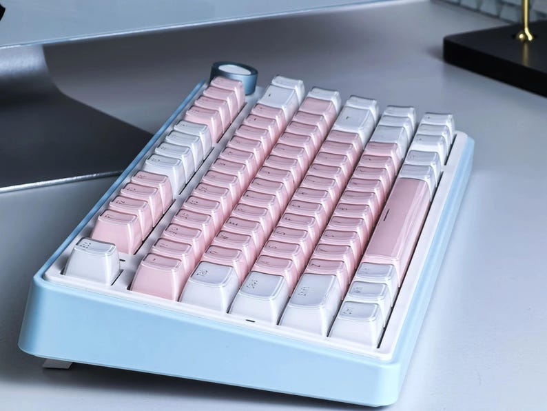 May include: A pastel-colored mechanical keyboard with a light blue frame. The keycaps alternate between white and pink, creating a soft, visually appealing aesthetic. The keyboard is designed for computer use.