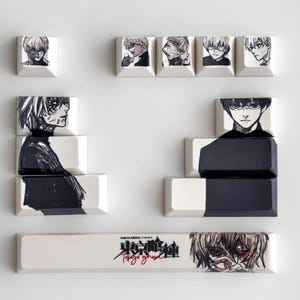 Pode incluir: Um conjunto de teclas personalizadas com ilustrações de anime em preto e branco. As teclas mostram retratos de personagens e o título "Tokyo Ghoul" em japonês e inglês. As teclas são brancas com obras de arte pretas.