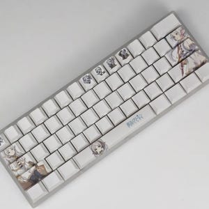May include: A white mechanical keyboard with custom keycaps featuring anime-style illustrations. The keycaps have various character designs and Japanese text. The keyboard has a silver frame and a standard QWERTY layout.