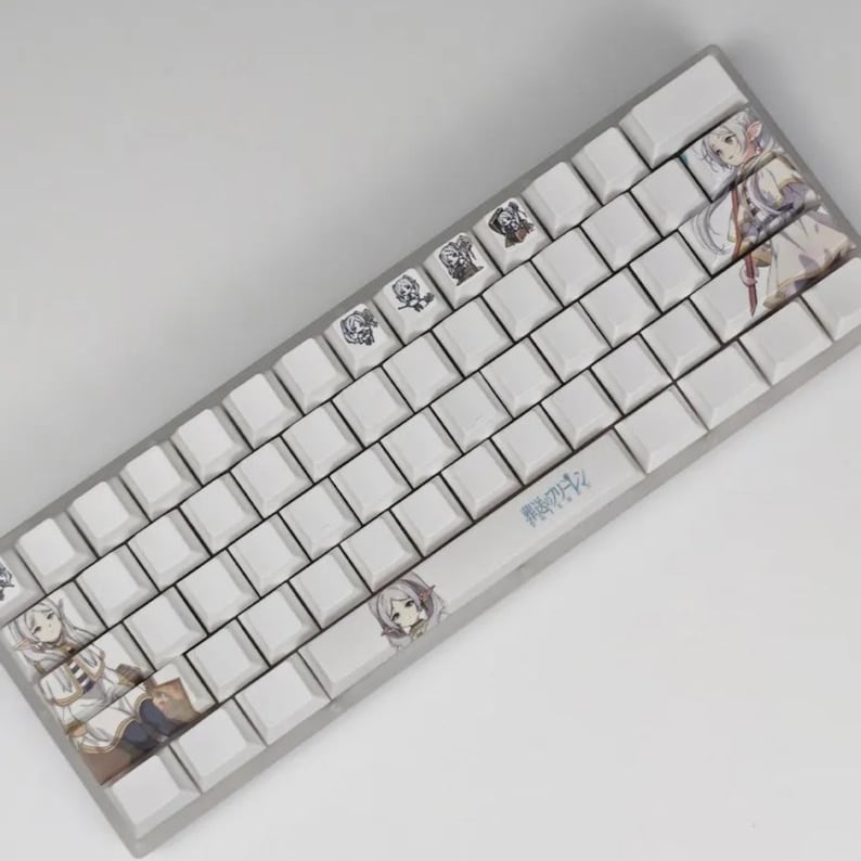 May include: A white mechanical keyboard with custom keycaps featuring anime-style illustrations. The keycaps have various character designs and Japanese text. The keyboard has a silver frame and a standard QWERTY layout.