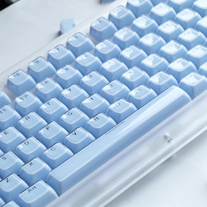 Puede incluir: Primer plano de un teclado mec&aacute;nico con teclas azul claro. Las teclas est&aacute;n dispuestas en una distribuci&oacute;n QWERTY est&aacute;ndar, con letras y s&iacute;mbolos blancos. El teclado tiene un marco blanco y una base azul claro.