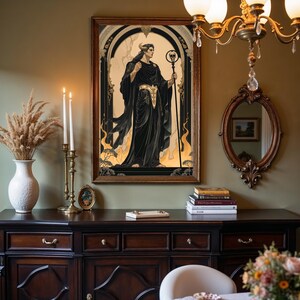 May include: A framed artwork depicts a figure in black robes holding a staff with a skull. The artwork has a gold and black color scheme, with a dark wooden frame. The image is displayed above a dark wooden cabinet.