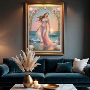 Op de afbeelding: Een ingelijst kunstwerk toont een vrouw in een roze jurk in de oceaan bij zonsondergang. Het schilderij in een gouden lijst hangt boven een tealkleurige bank met kussens. Een gouden vaas met pampasgras en kaarsen maakt de sc&egrave;ne compleet.
