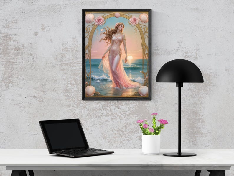 Op de afbeelding: Een ingelijste kunstdruk toont een vrouw in een roze jurk in de zee bij zonsondergang. Het kunstwerk heeft een gouden boog met rozen en schelpen. De print staat op een muur boven een wit bureau met een laptop, een lamp en een kleine potplant.
