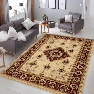 May include: A rectangular area rug featuring a cream-colored field with a central dark red medallion and matching border. The design includes repeating circular motifs and geometric patterns throughout the surface, creating a symmetrical layout.
