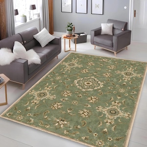 May include: A rectangular area rug featuring a sage green background with a repeating pattern of beige and cream floral medallions and scrolling vine motifs. The rug has a finished edge border and is positioned on a light-colored floor surface.
