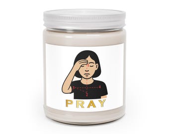 May include: A beige candle jar with a white label featuring a graphic of a person praying. The word "PRAY" is printed in gold below the graphic. The jar has a silver lid.