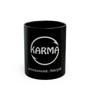 May include: Black ceramic mug with the word "Karma" in a white circular design with arrows. The phrase "pronounced: /fek/yōō" is printed below the design. The mug is cylindrical and has a glossy finish.