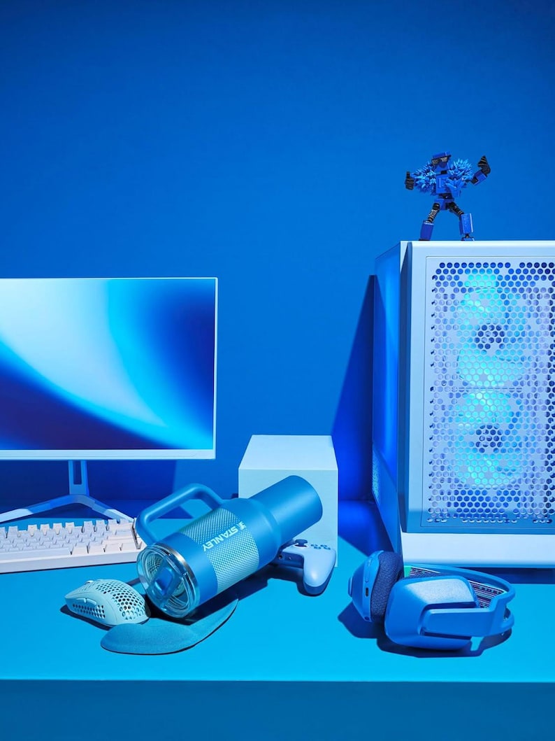 Puede incluir: Una configuraci&oacute;n de juego azul con una computadora, monitor, teclado, rat&oacute;n, auriculares y una botella de agua Stanley. Una figura de acci&oacute;n azul est&aacute; encima de la torre de la computadora. El conjunto est&aacute; sobre una superficie azul.