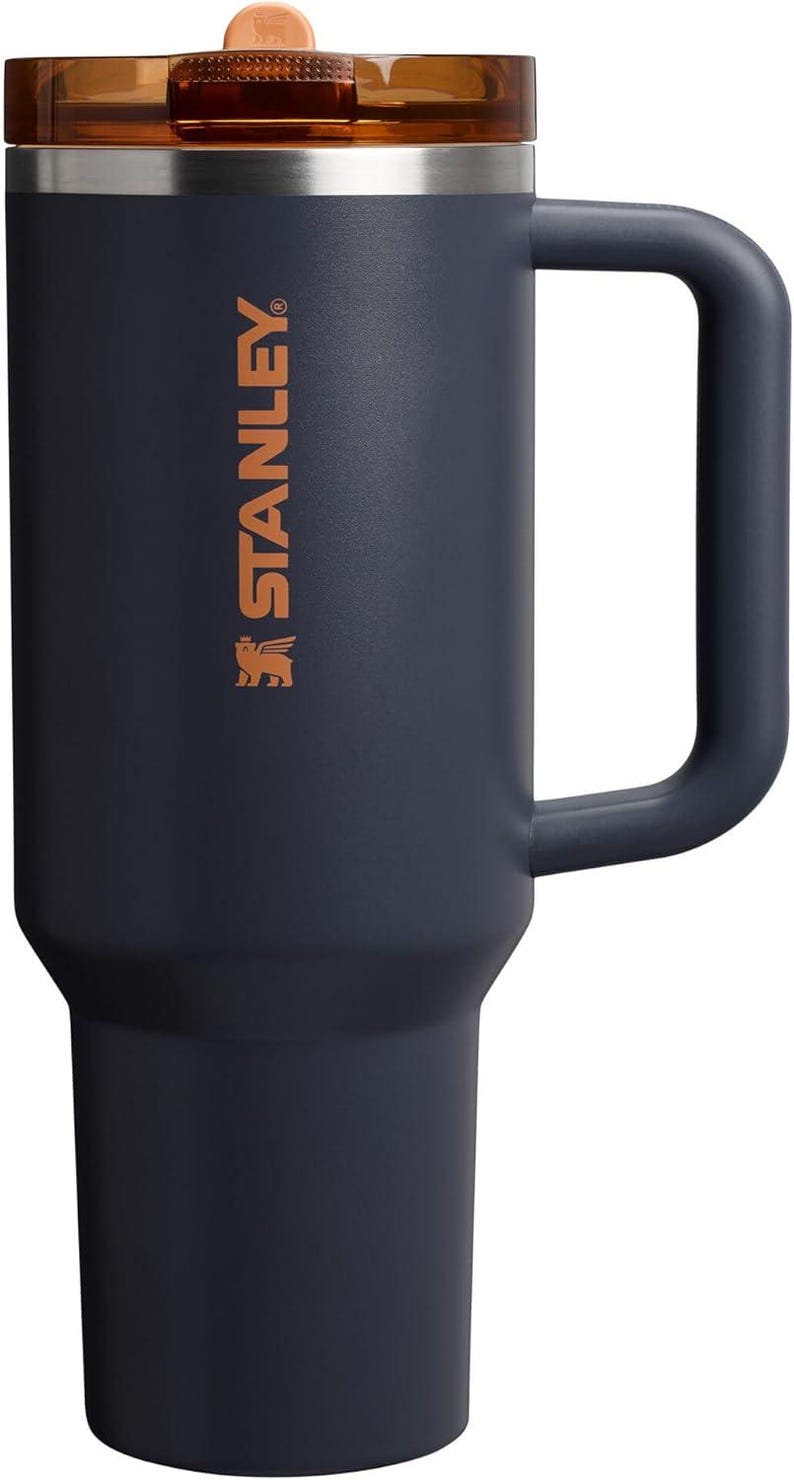 Puede incluir: Un termo de color azul marino con asa y tapa marr&oacute;n. El termo tiene la palabra "STANLEY" impresa en color cobre en el lateral. El termo est&aacute; dise&ntilde;ado para mantener las bebidas calientes o fr&iacute;as durante horas.