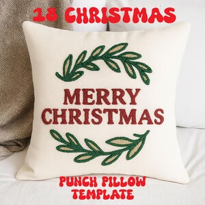 Op de afbeelding: Crèmekleurig vierkant kussen met de rode tekst "MERRY CHRISTMAS", omringd door groen en goud geborduurde bladeren. De tekst "18 CHRISTMAS" staat erboven en "PUNCH PILLOW TEMPLATE" eronder, beide in rood.