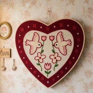 Puede incluir: Adorno de pared en forma de corazón con borde rojo y centro crema. El centro presenta dos pájaros, flores y un diseño floral. También se ven una pequeña rosa enmarcada y un letrero de madera "Love".