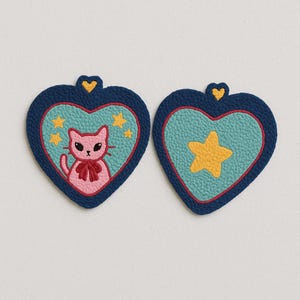May include: Two heart-shaped coasters. One features a pink cat with a red bow, surrounded by yellow stars, and the other has a yellow star. Both have a blue border and a yellow heart at the top.