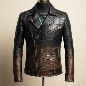 Könnte beinhalten: Schwarze und braune Lederjacke mit Krokodilhautstruktur. Die Jacke hat einen Reißverschluss, mehrere Taschen und goldfarbene Hardware. Die Ärmel haben einen Farbverlauf, der von Schwarz zu Braun übergeht. Das Etikett lautet "CHOCO BLVD."